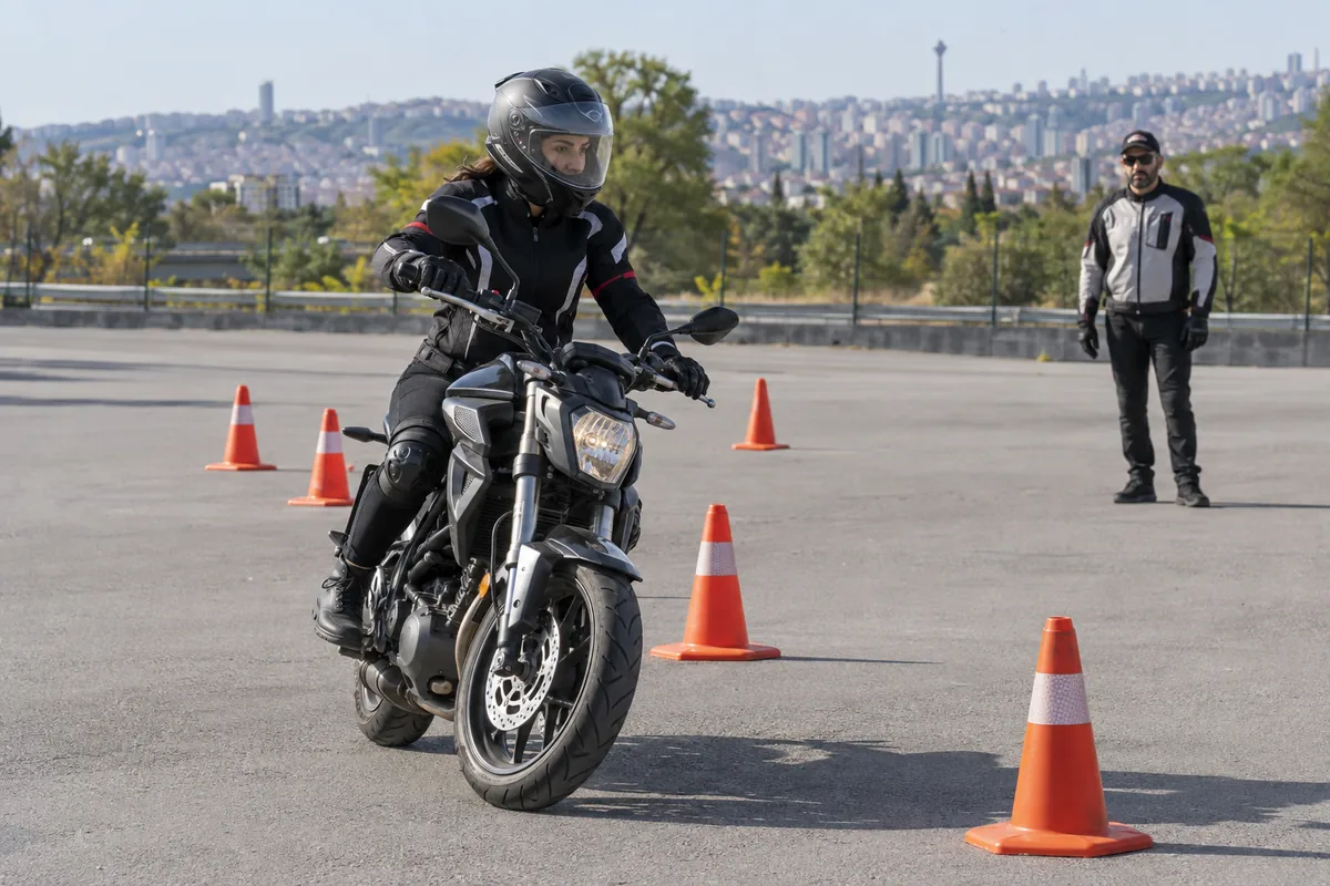 Kapalı eğitim alanında koruyucu ekipmanla düşük hız denge çalışması yapan motosiklet sürücüsü, temsili görsel